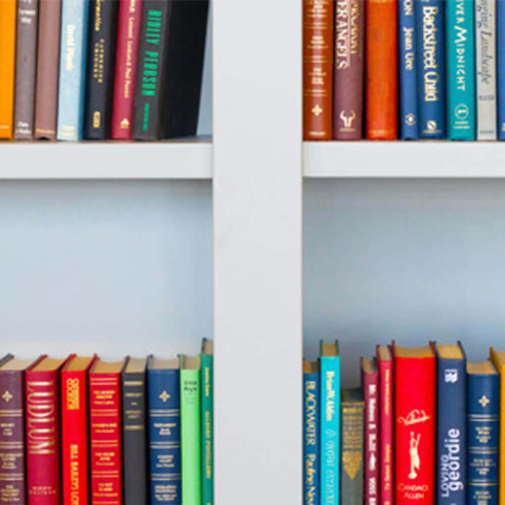 Ein weißes Bücherregal, das an einer Wand befestigt ist, gefüllt mit einer Vielzahl von Büchern in unterschiedlichen Farben und Größen.