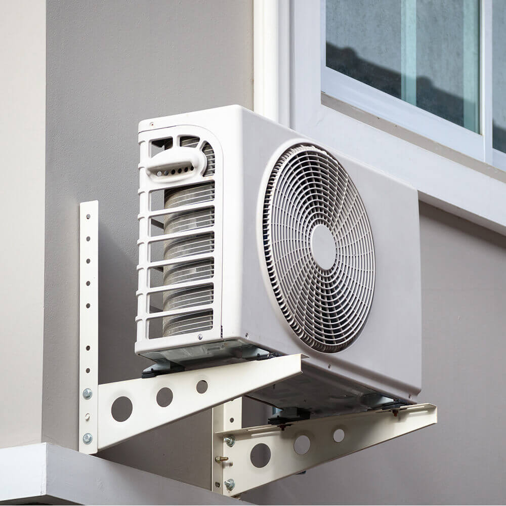 Eine Außenklimaanlage, die an der Außenwand eines Gebäudes montiert ist. Die Klimaanlage ist sicher auf robusten Metallhalterungen befestigt, die an der Wand verschraubt sind.