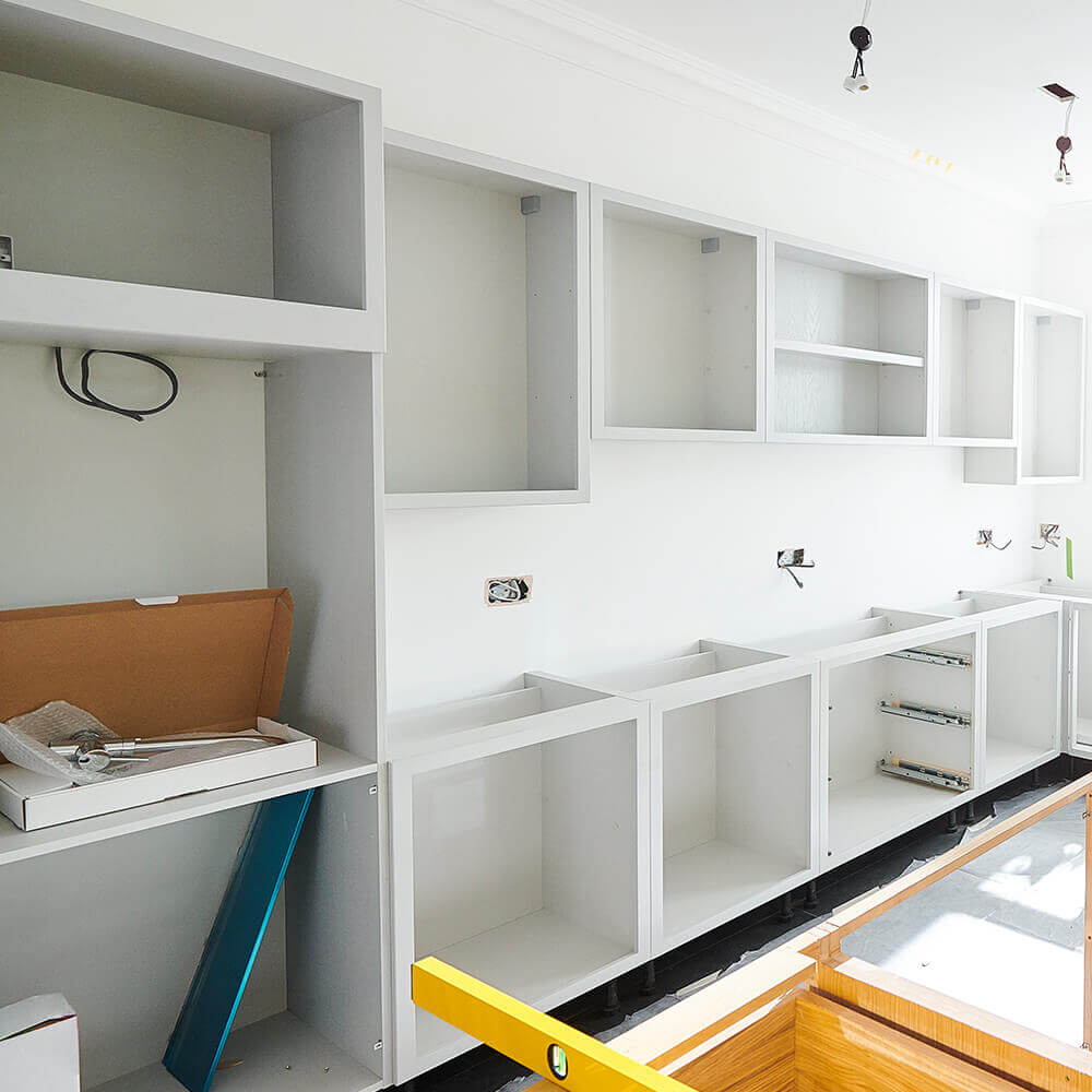 Eine Küche im Bau, mit leeren weißen Schränken, die an der Wand befestigt sind. Die Schränke sind sicher montiert und bieten Platz für Geräte und Stauraum.