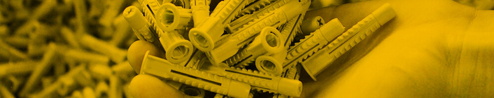 Nahaufnahme einer Hand, die mehrere gelbe Dübel hält, mit einer großen Menge weiterer Dübel im Hintergrund.