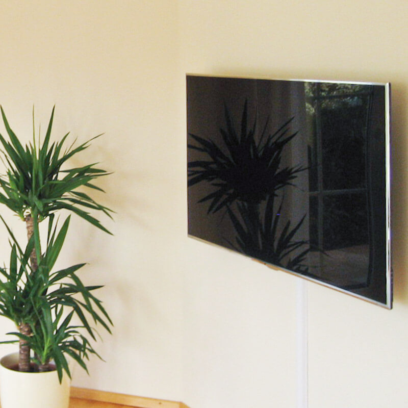 Ein Flachbildfernseher, der an einer beigen Wand montiert ist. Der Fernseher ist sicher an der Wand befestigt und darunter sind die Kabel ordentlich verlegt.
