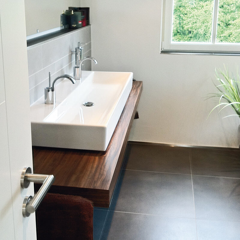 Ein modernes Badezimmer mit einem großen rechteckigen Waschbecken, das auf einer hölzernen Waschtischplatte montiert ist. Die Waschtischplatte ist sicher an der Wand befestigt und bietet eine stilvolle und stabile Lösung für die Befestigung des Waschbeckens.