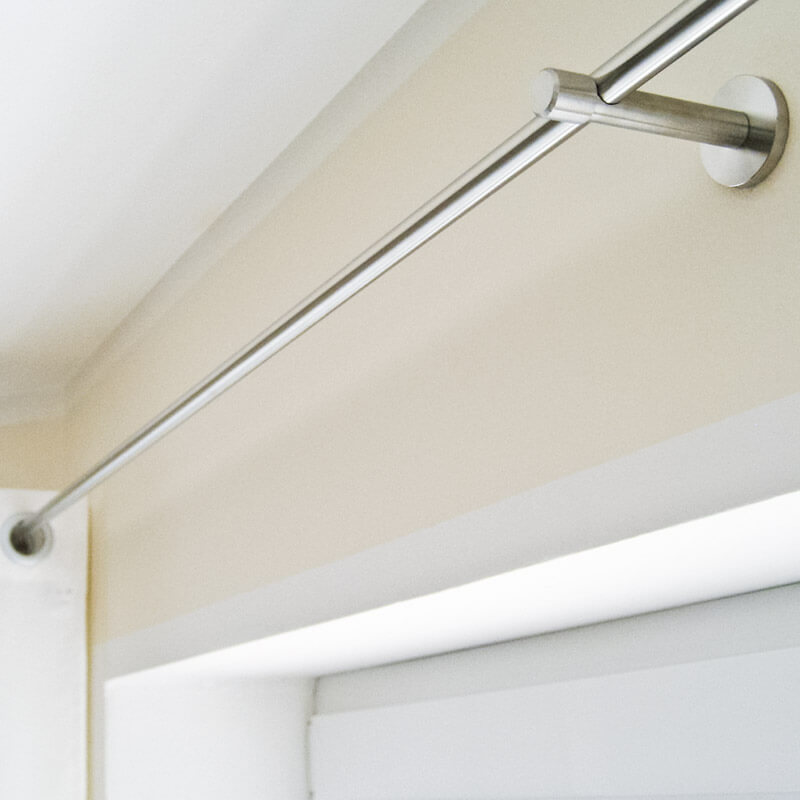 Eine silberne Gardinenstange aus Metall, die über einem Fensterrahmen befestigt ist. Die Gardinenstange ist mit stabilen Wandhalterungen sicher an der Wand montiert.