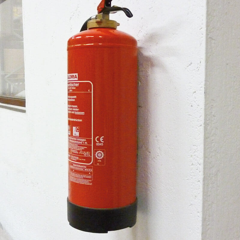 Ein roter Feuerlöscher, der an einer weißen Wand befestigt ist.