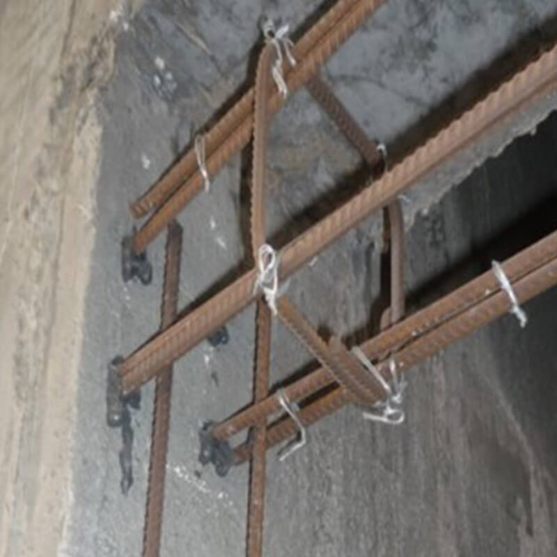 Eine Baustelle, an der Bewehrungsstäbe mit chemischen Mörteln in einer Betonwand verankert sind. Die Bewehrungsstäbe sind mit Draht gesichert und bereit für die Betonierung, um die strukturelle Integrität der Wand zu erhöhen.