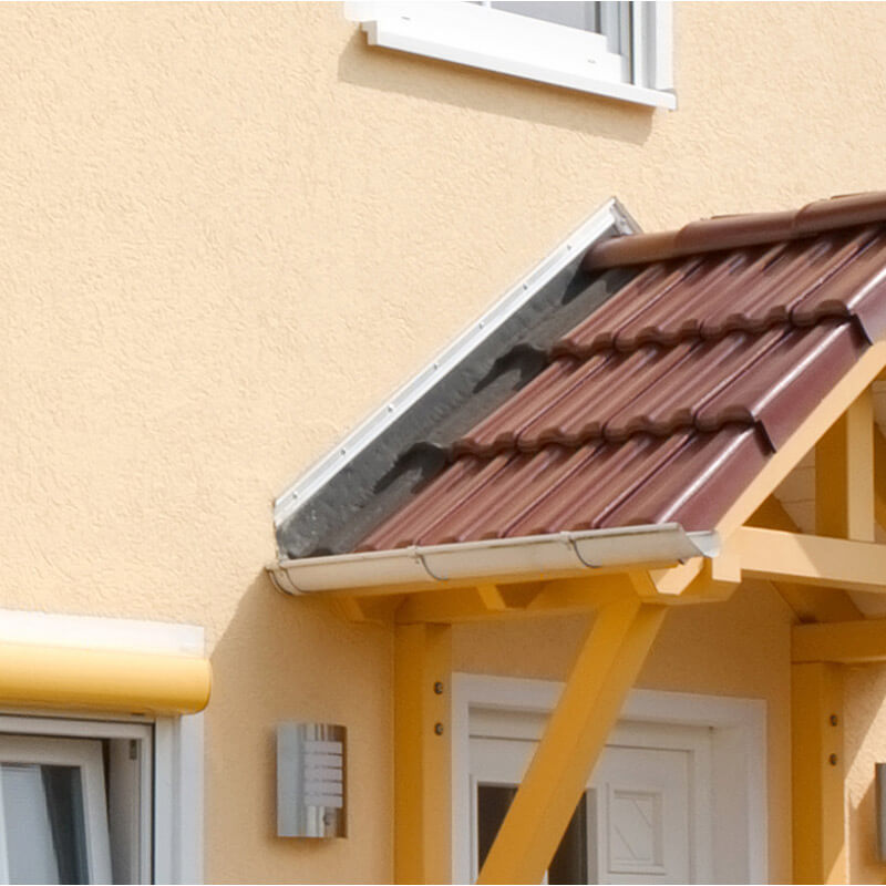 Ein kleines Vordach mit roten Dachziegeln über einem Hauseingang, das an einer gedämmten Hauswand befestigt ist. Die Befestigung des Vordachs wurde mit CELO-Dämmstoffdübeln durchgeführt, um eine stabile und sichere Montage an der gedämmten Fassade zu gewährleisten.