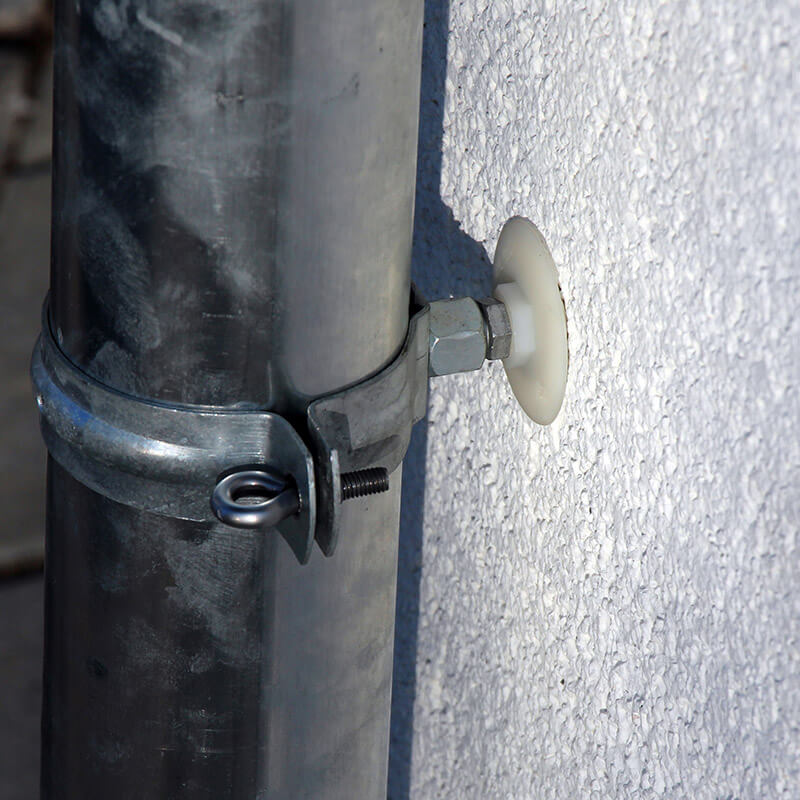 Eine metallene Rohrschelle, die an einem großen Rohr befestigt ist und mit einem CELO-Dämmstoffdübel sicher an einer verputzten Wand verankert ist. Der IPL 95DS sorgt für eine stabile und langlebige Befestigung des Rohres an der gedämmten Wandoberfläche.