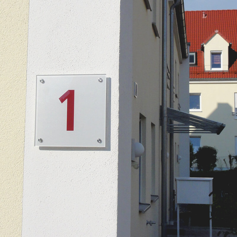 Ein weißes Hausnummernschild mit der Nummer 1, das an einer verputzten und gedämmten Hauswand befestigt ist. Die Befestigung des Schildes wurde mit CELO-Dämmstoffdübeln durchgeführt, um eine stabile und sichere Montage an der gedämmten Fassade zu gewährleisten.