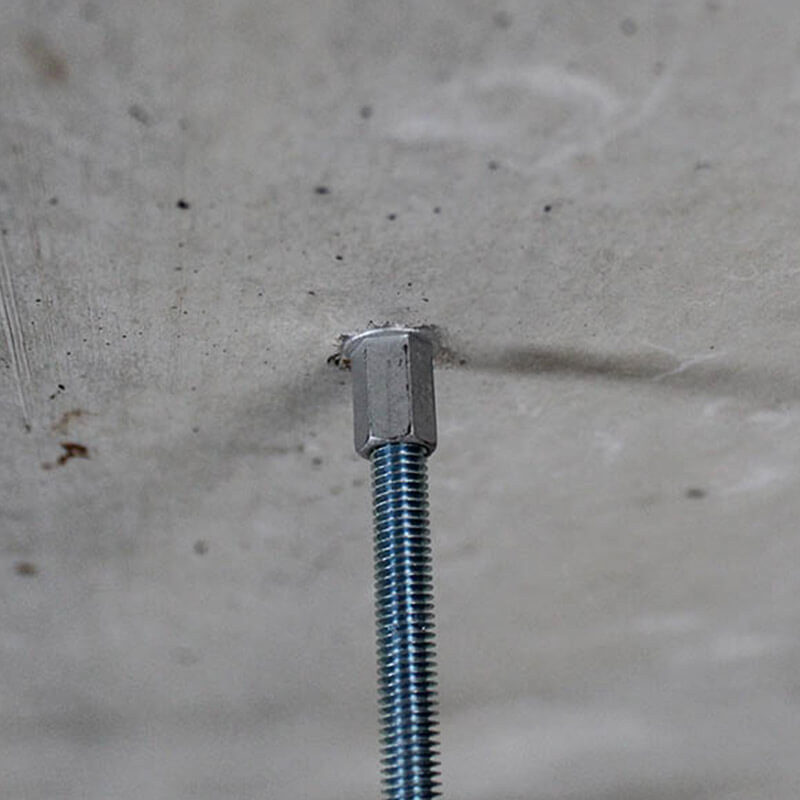 Nahaufnahme einer Metallgewindestange, die in eine Betonoberfläche mithilfe einer Betonschraube eingeschraubt ist. Die Gewindestange ist sicher befestigt und zeigt eine präzise Installation in der Betondecke.