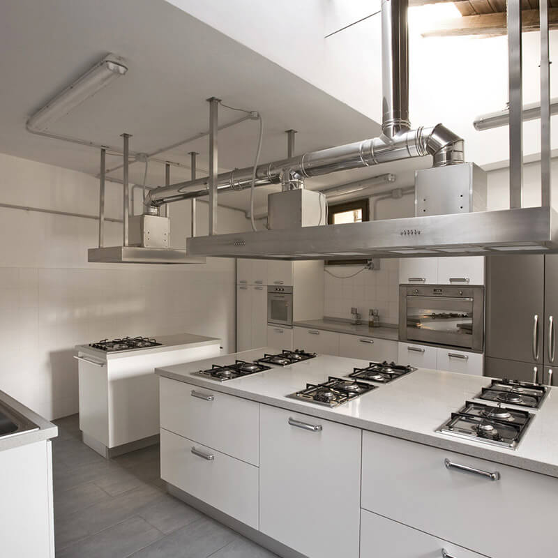 Schwere Abluftrohre die in einer Industrieküche an der Decke abgeängt sind mittels Schwerlastbefestigungen wie Bolzenankern.