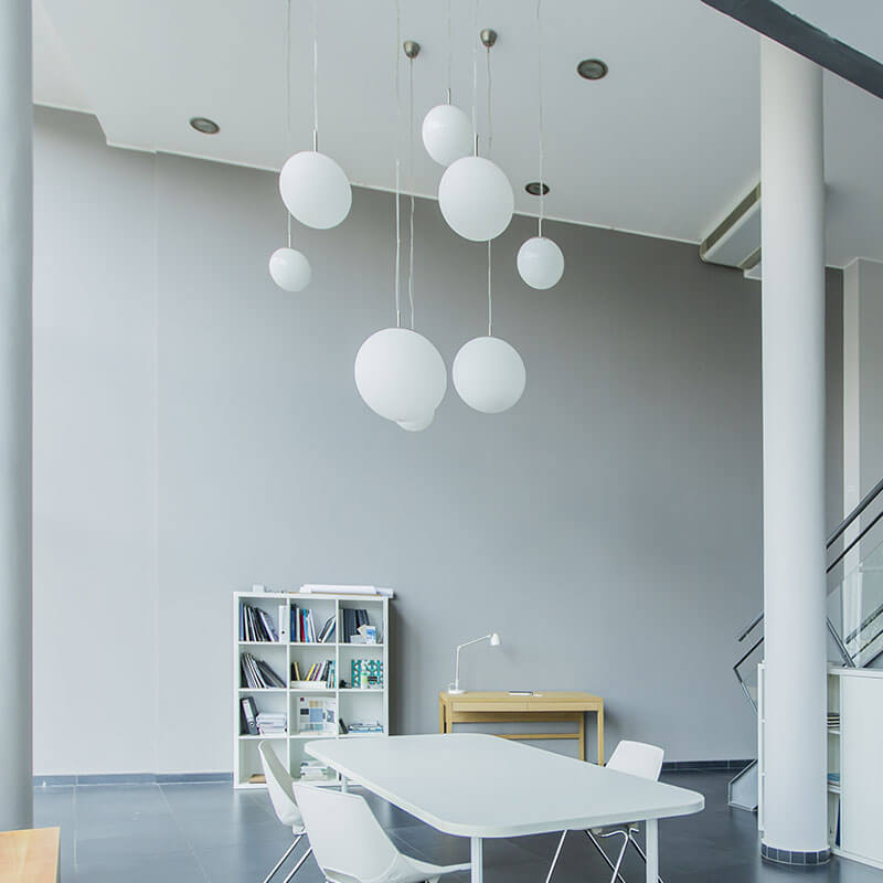 Ein modernes Büro mit einer hohen Decke, an der mehrere weiße Pendelleuchten in unterschiedlichen Höhen befestigt sind.