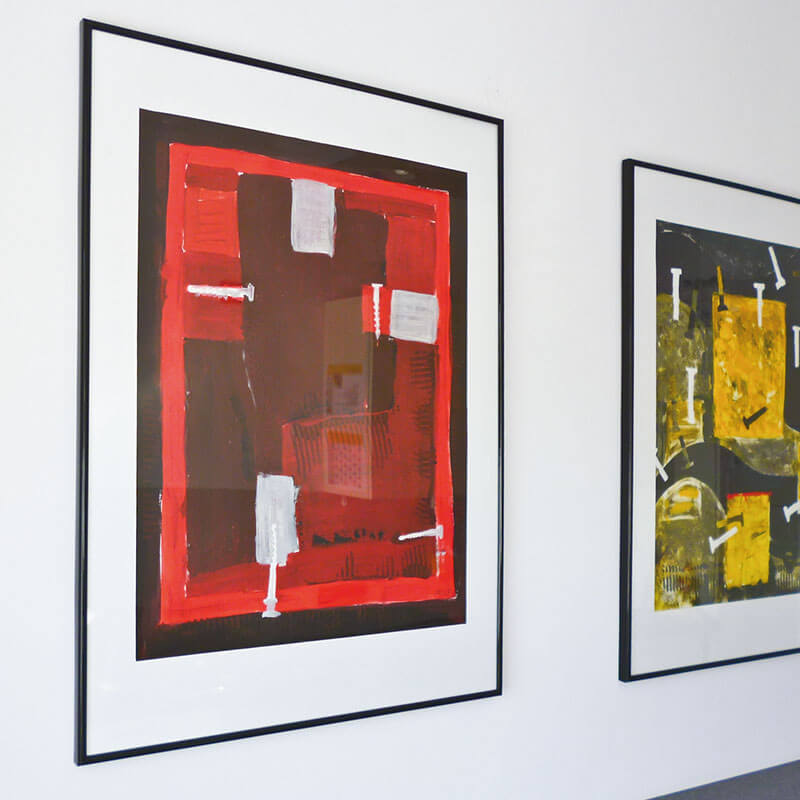 Zwei abstrakte Kunstwerke in schwarzen Rahmen, die nebeneinander an einer weißen Wand hängen.