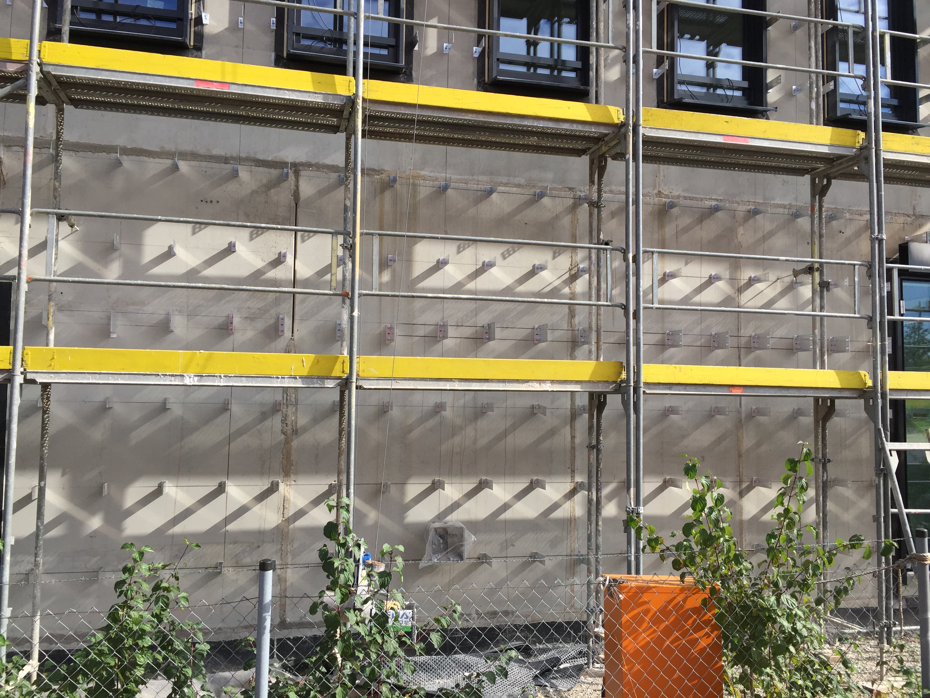 Ein Foto einer Baustelle mit einem Gerüst und einer Wand, an der zahlreiche Verankerungen für die Installation von Fassadenelementen angebracht sind.