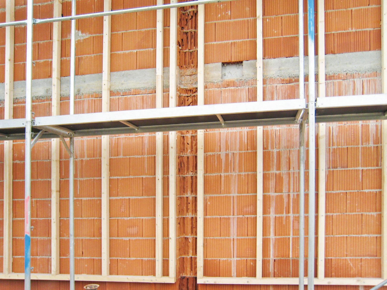 Ein Foto einer Baustelle mit einem Ziegelmauerwerk, das mit vertikalen und horizontalen Latten für die Montage von Dämmmaterial vorbereitet ist.