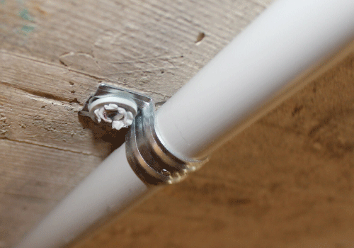 Ein weißes Rohr wird mithilfe des ETA-zugelassenen Metallclips PFT an einer Betondecke montiert