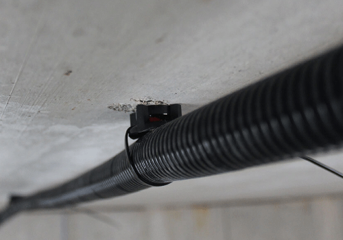 Das Anwendungsbild zeigt den schwarzen ETA-zugelassenen Kabelbinderbefestiger TBB, an dem mithilfe eines Kabelbinders ein Leerrohr befestigt ist